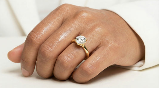 Hand wearing a gold ring with a diamond on a light background