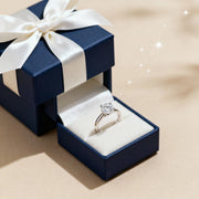 Diamond ring in an open blue box with a white ribbon on a beige background